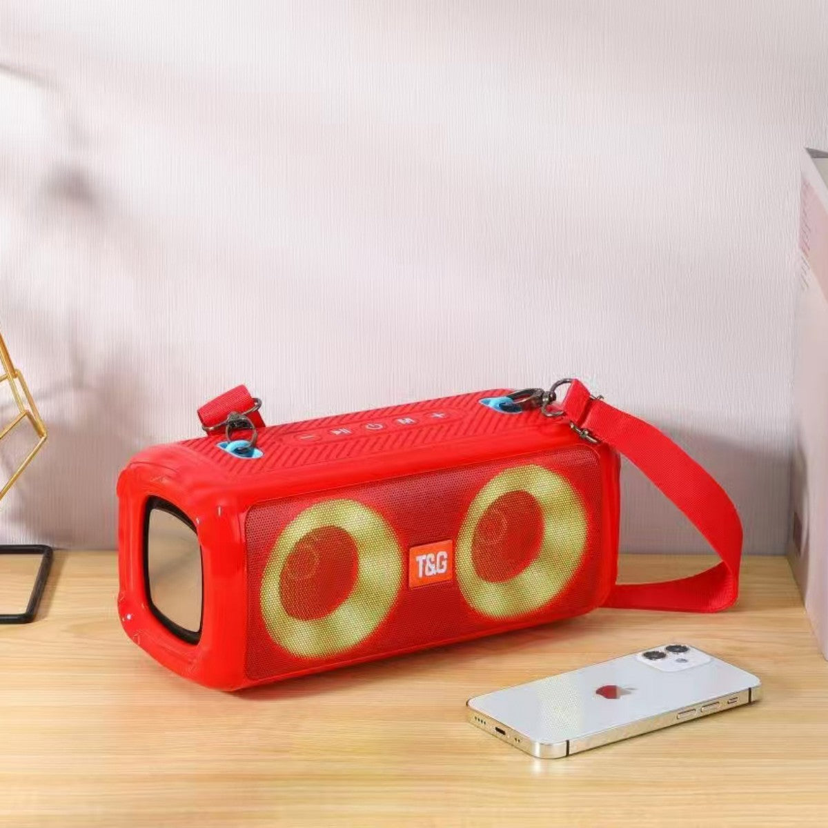 Red T&G TG641 RGB Wireless Bluetooth Speaker with 5W*2 Bass and yellow LED lights, shown on a desk beside a smartphone for scale.