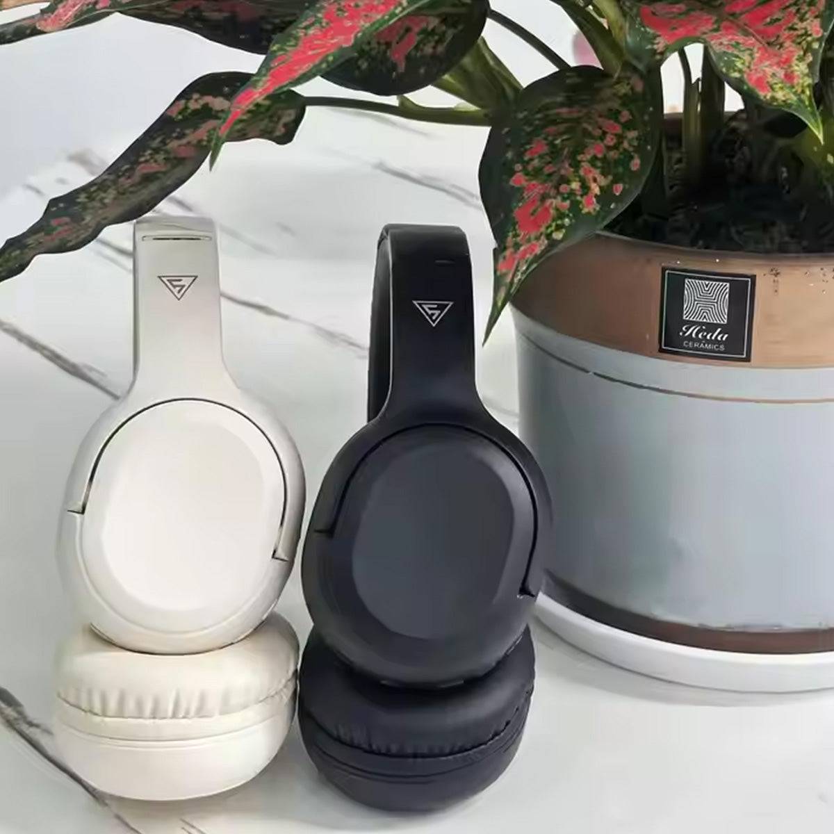 Black and white DOQAUS APEX5 Wireless Headphones placed beside a potted plant, showcasing stylish design and color options.