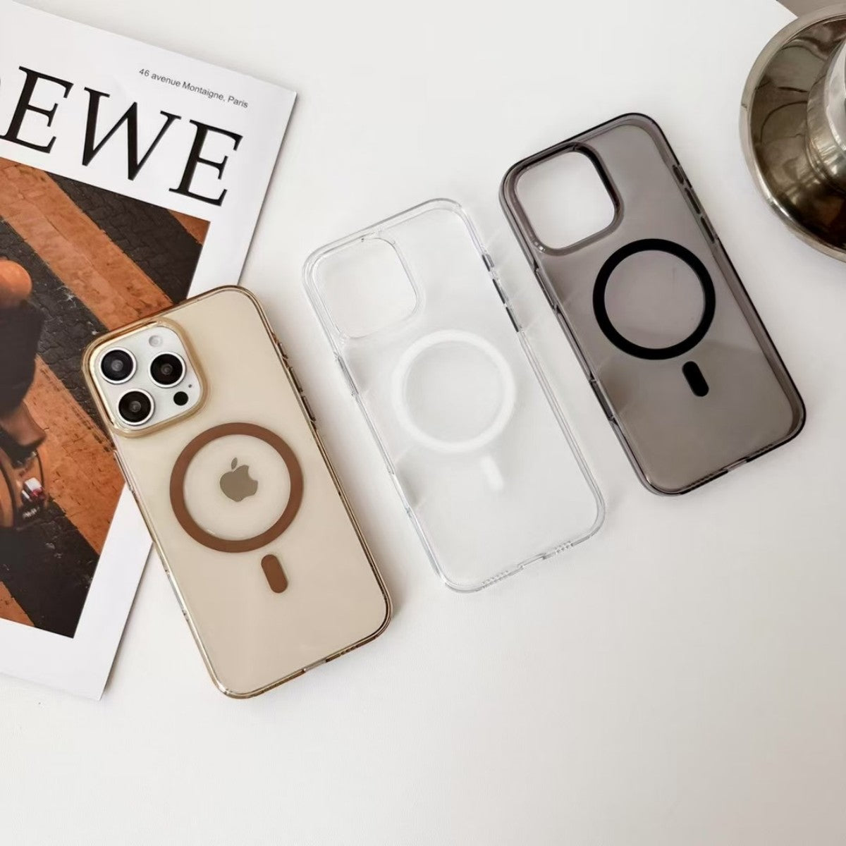 AuraGuard Series iPhone Clear Cases in three colors laid flat beside an iPhone and magazine, highlighting stylish MagSafe compatibility.