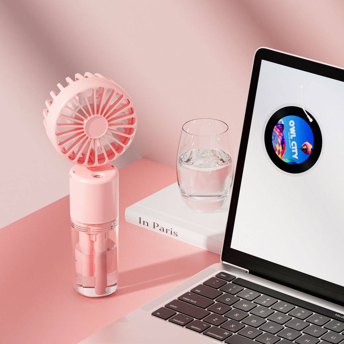 Pink F2 misting fan on a desk next to a laptop and water glass. Aesthetic and practical for workspace and home cooling solutions.